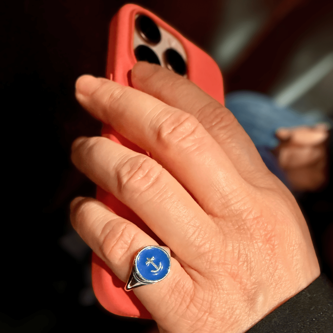 Hand wearing Silver Delta Gamma Anchor Signet Ring, holding an iPhone in a bright melon colored case on a dark background.