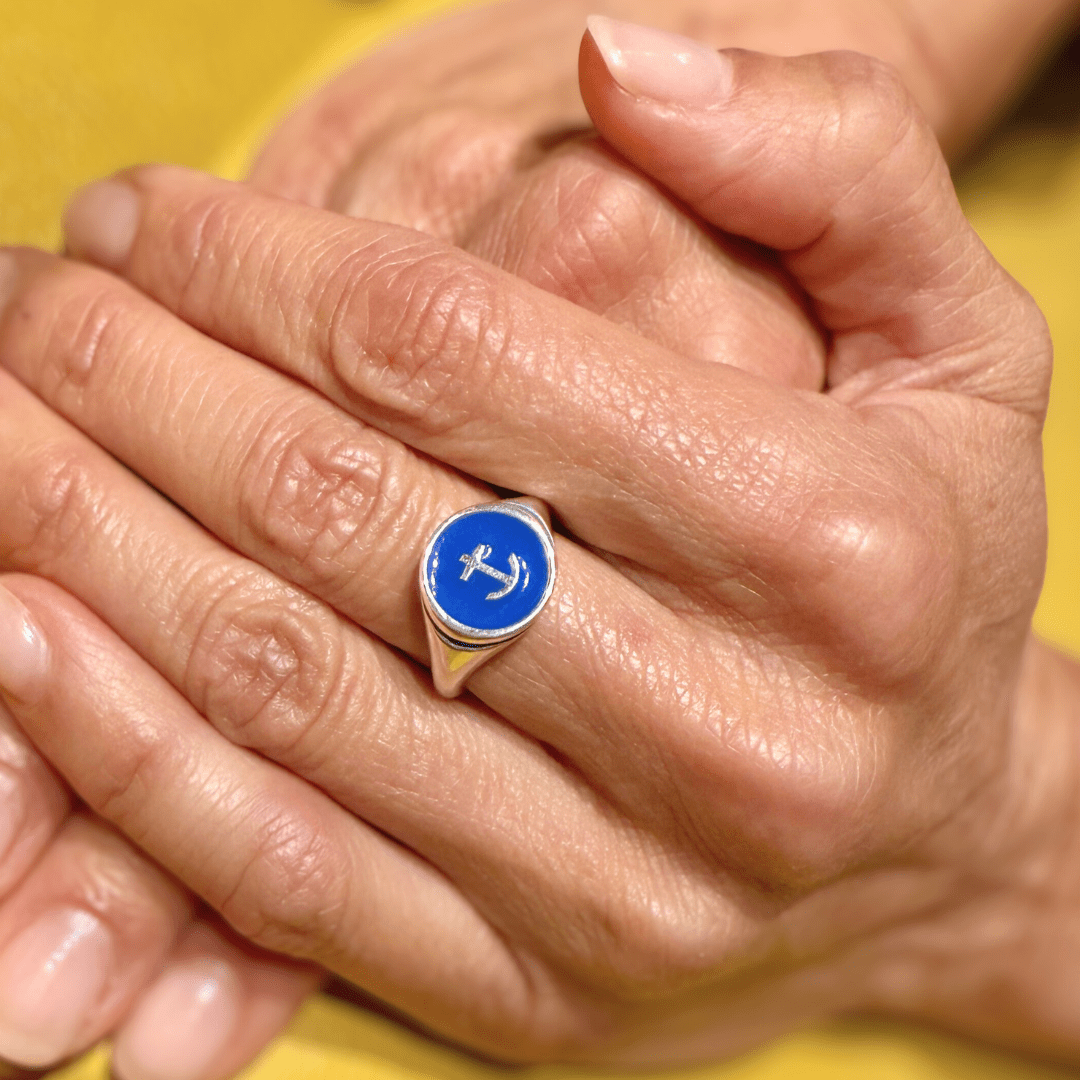 Hand wearing Silver Delta Gamma Anchor Signet Ring, folded over other hand, resting on a yellow tabletop.