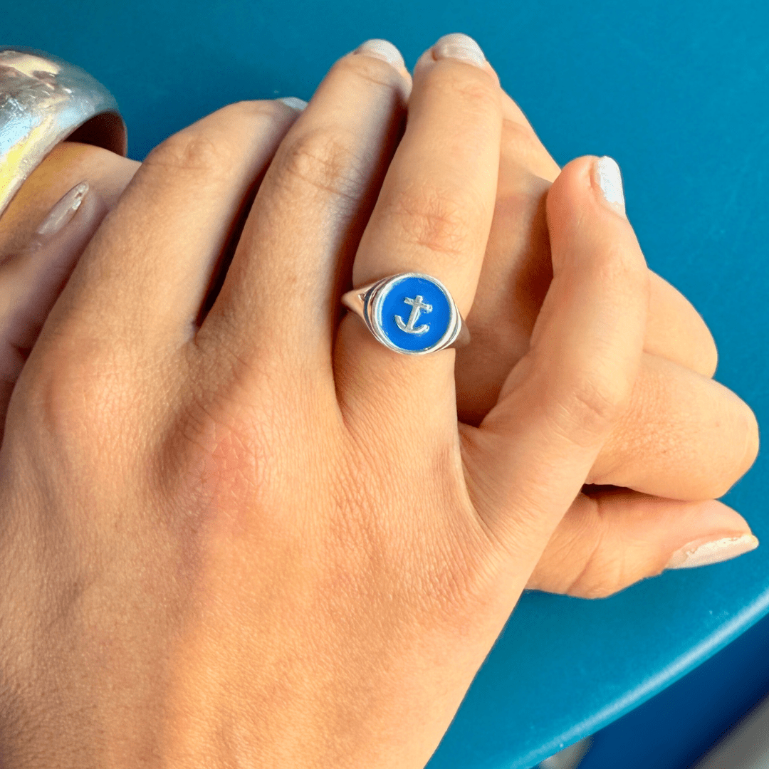 Hand wearing Silver Delta Gamma Anchor Signet Ring, resting on a blue tabletop.